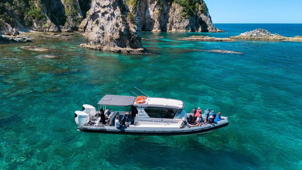 A boat with passengers on a clear turquoise sea, surrounded by rocky cliffs. 4