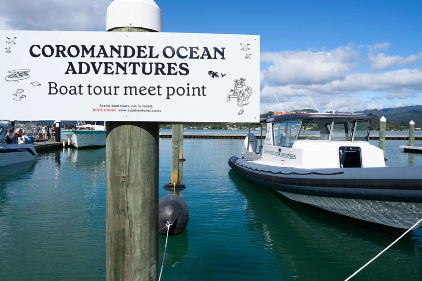 A boat docked at a pier with a sign for Coromandel Ocean Adventures. 5