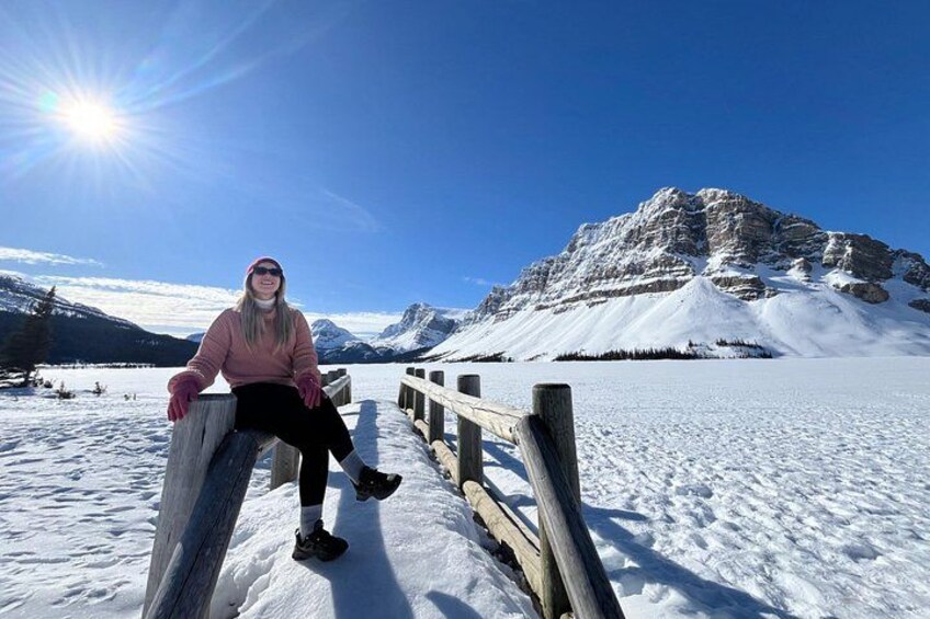 Een persoon zit op een houten steiger in een besneeerd landschap met bergen op de achtergrond. 2