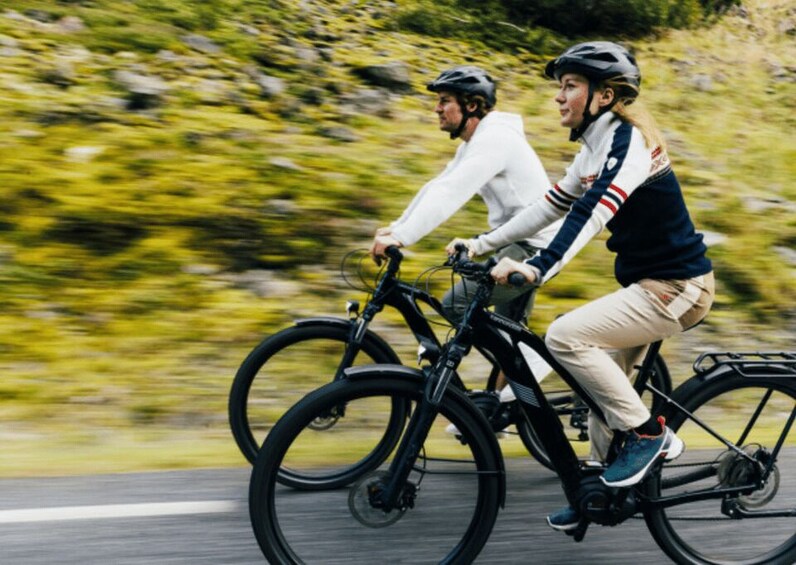 Two cyclists on a road with blurred greenery in the background. 1