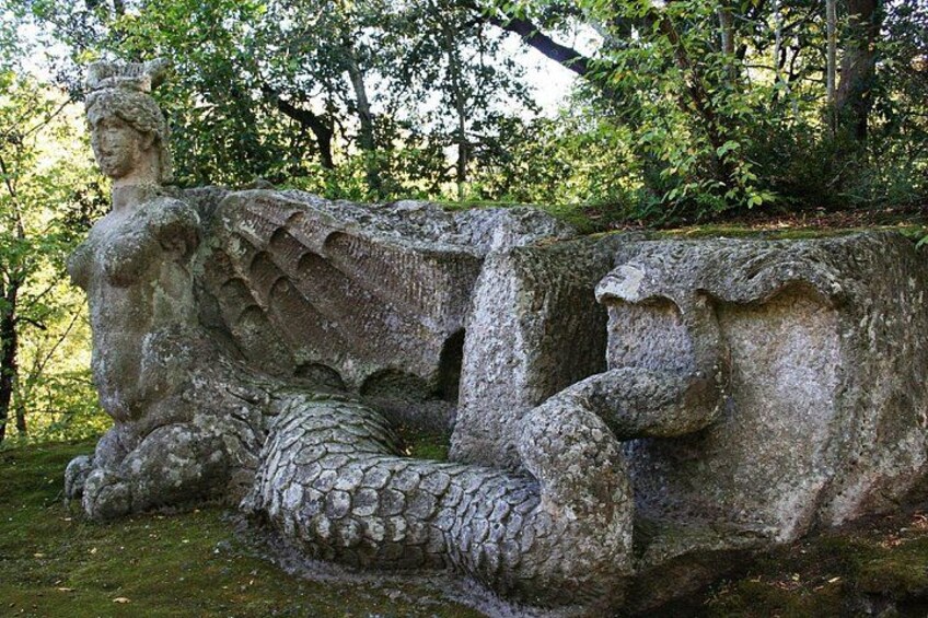 A stone sculpture of a woman and a snake in a forest. 3