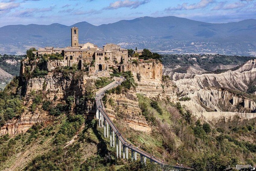 A historic stone building on a cliff, a bridge, and a mountainous landscape. 1