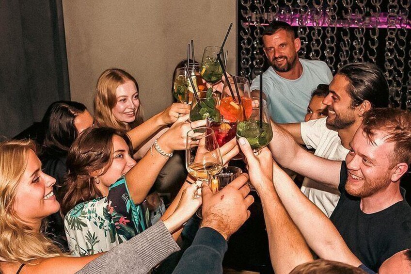 A group of people toasting with drinks in a bar setting. 2