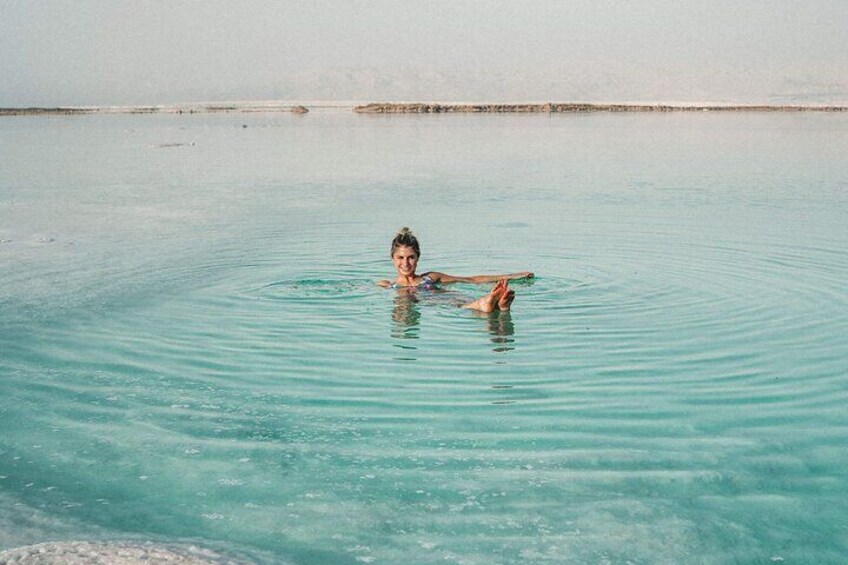 A person floating in a clear blue body of water with a sandy beach in the background. 2