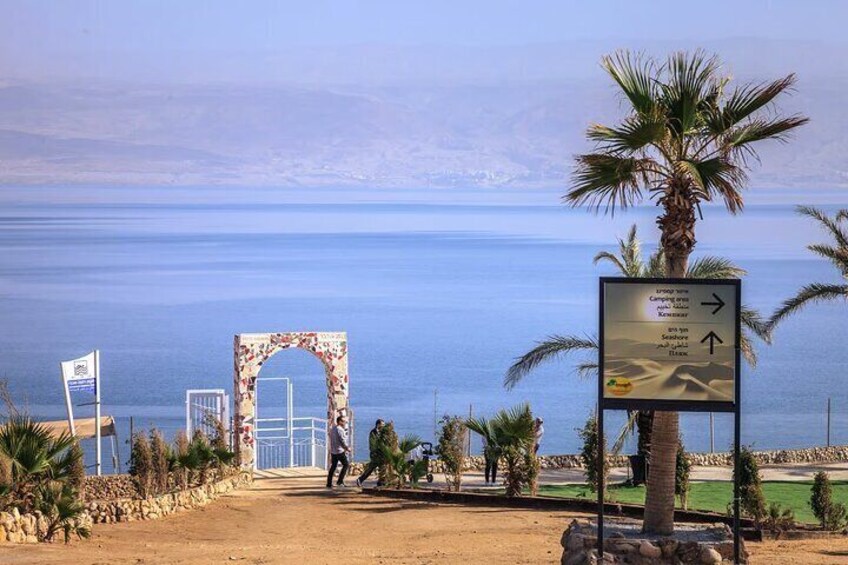 A coastal pathway with a palm tree, a signpost, and a decorative archway. 4