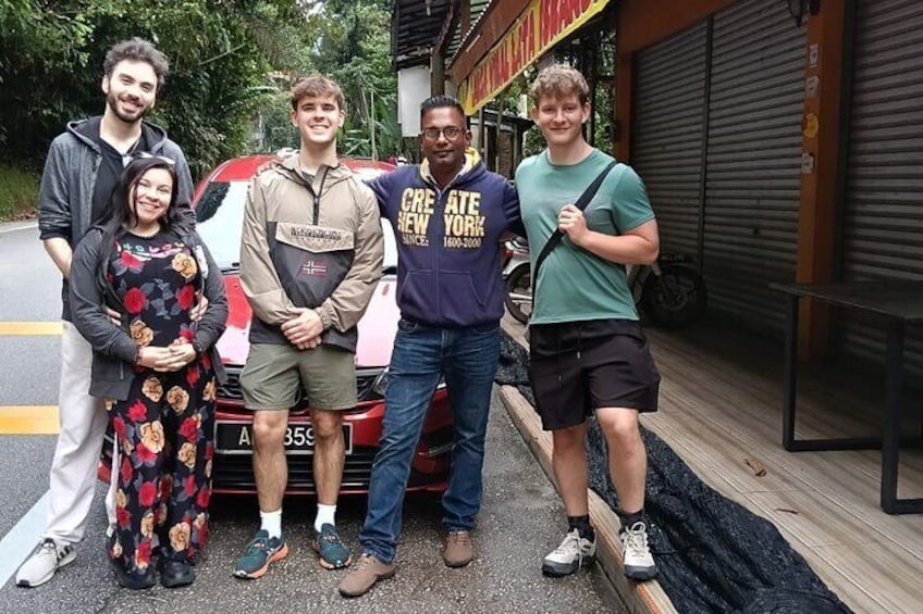 A group of people standing in front of a red car with a license plate. 3
