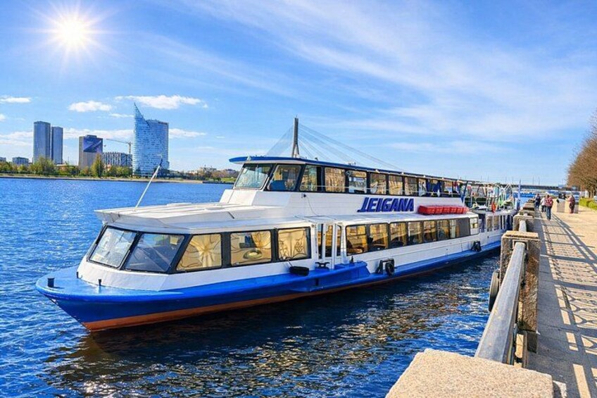 Un bateau bleu et blanc, baptisé « LEIGANA », navigue sur une rivière, avec la silhouette d’une ville en arrière-plan. 3