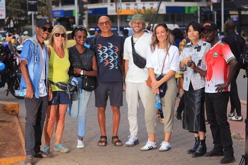 A group of people standing on a sidewalk with a street and parked motorcycles in the background. 4