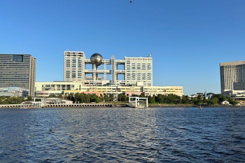 A waterfront cityscape with modern buildings, a clear sky, and calm water. 2
