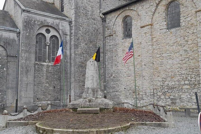 A stone building with flags, a fountain, and a statue. 2