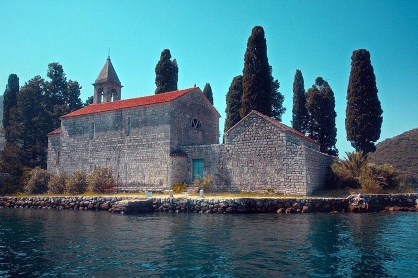A stone building with a red roof by a body of water, surrounded by trees. 3