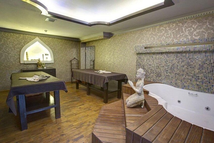 Een badkamer met een houten vloer, een bad, een massagetafel, een wastafel met spiegel en een decoratief beeld. 4