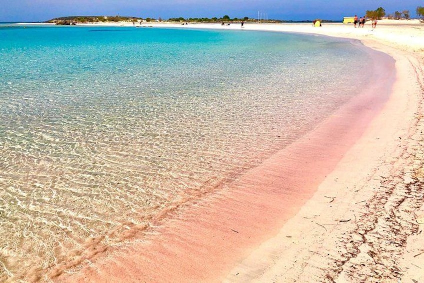 Une plage à l’eau turquoise et limpide, une zone de sable rose et quelques personnes visibles au loin. 1
