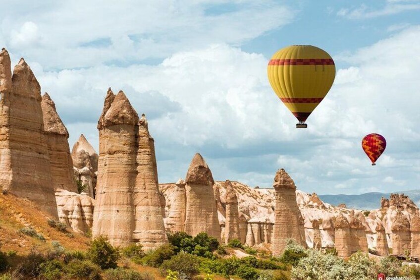 A landscape with tall, narrow rock formations and two hot air balloons in the sky. 5
