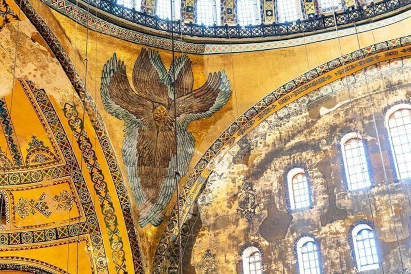 Un mosaico de un águila sobre fondo amarillo con diseños intrincados y parte de la fachada de un edificio. 2