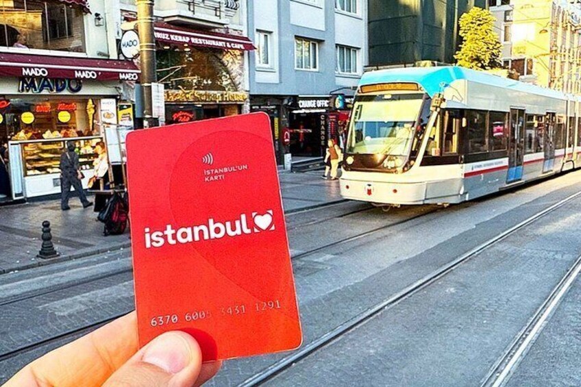A tram on tracks, a red card with 'istanbul' and a heart symbol, and storefronts in the background. 5