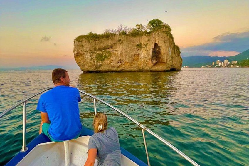 Una barca con due persone, un promontorio roccioso e edifici sullo sfondo. 4