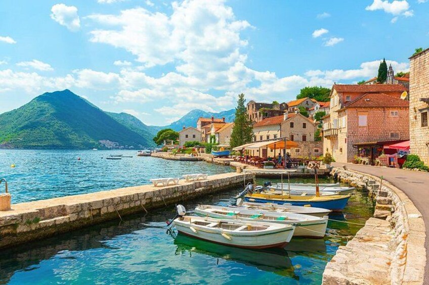 A coastal town with boats docked along the waterfront, stone buildings, and a mountain in the background. 3