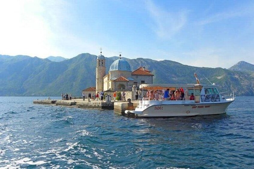 A boat with passengers docked at a pier, a church with a dome, and mountains in the background. 5