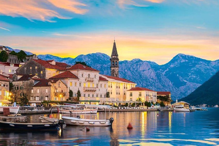 A waterfront town with historic buildings, a church tower, and mountains in the background. 4