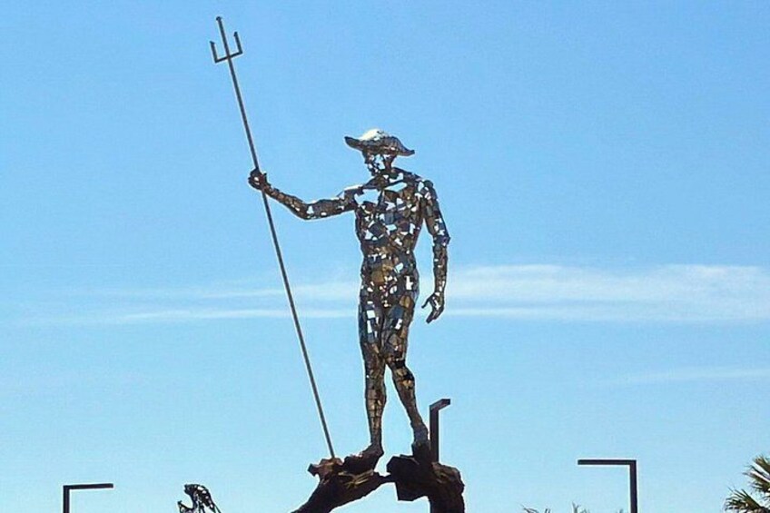 En metalkunst af en figur, der holder et trident, stående på en platform med en klar himmel i baggrunden. 4
