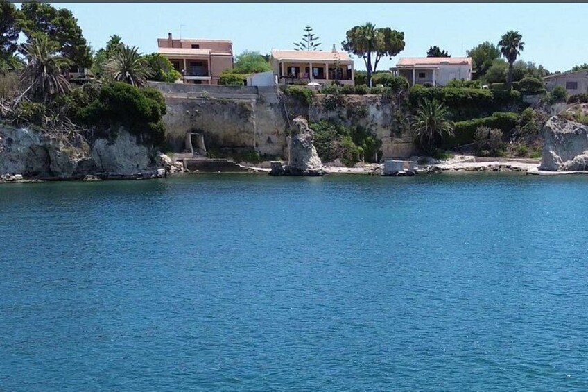 A coastal area with buildings, rocky cliffs, and a calm sea. 2
