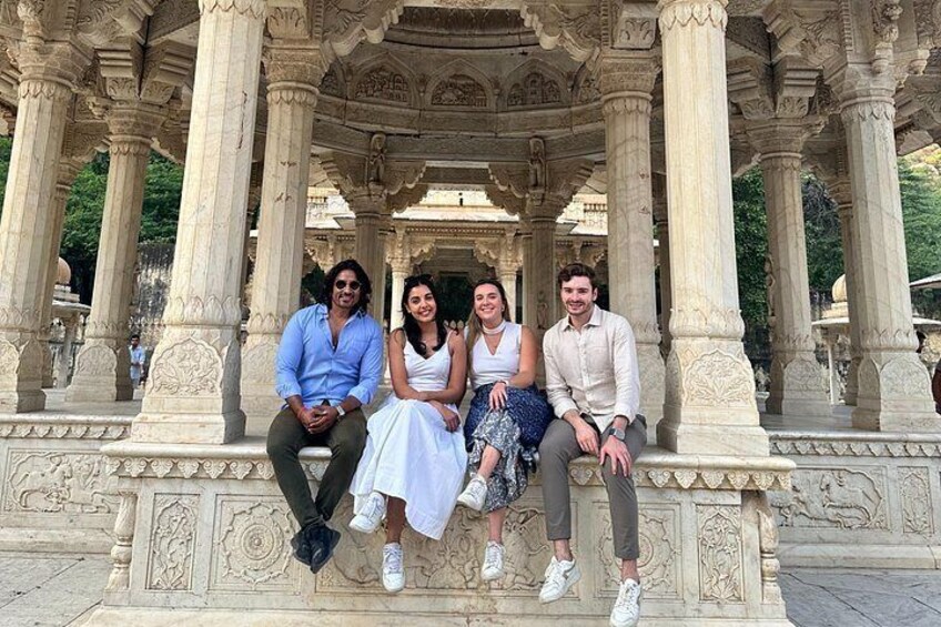 Four people sitting on a stone bench under a pavilion with intricate carvings. 5