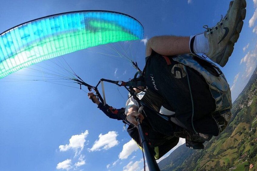 A person paragliding with a blue and green canopy, wearing a helmet, and holding onto the control bar. 4