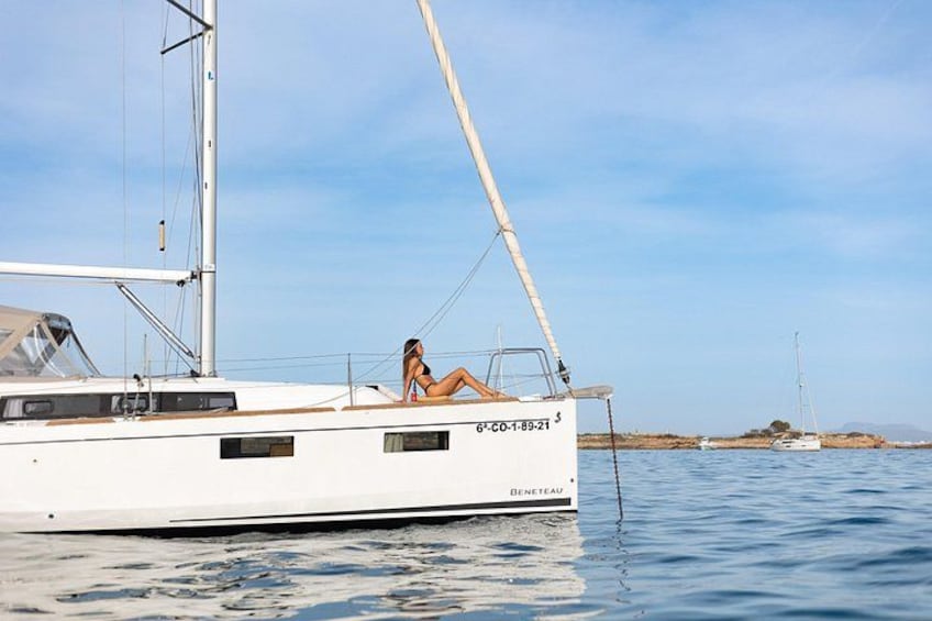 Ein Segelboot mit einer Person auf dem Deck, ruhiges Wasser und eine entfernte Küste. 2