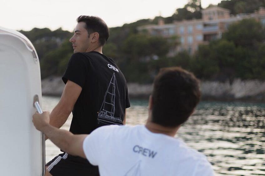 Una persona con camisa negra que tiene la palabra 'CREW' en la espalda, parada en un bote cerca de un muelle con edificios al fondo. 5