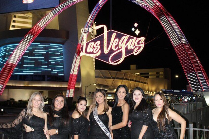Een groep mensen voor een neonbord met de tekst 'City of Las Vegas', met een grote bogenstructuur op de achtergrond. 3