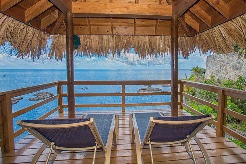 A wooden deck with two lounge chairs overlooking a body of water. 1