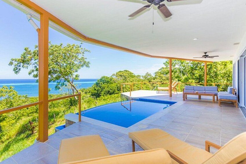 An infinity pool with a view of the ocean, outdoor furniture, and a ceiling fan. 2