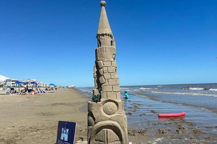 Una playa arenosa con una torre de piedra, un bote de remo rojo y tiendas de campaña al fondo. 2
