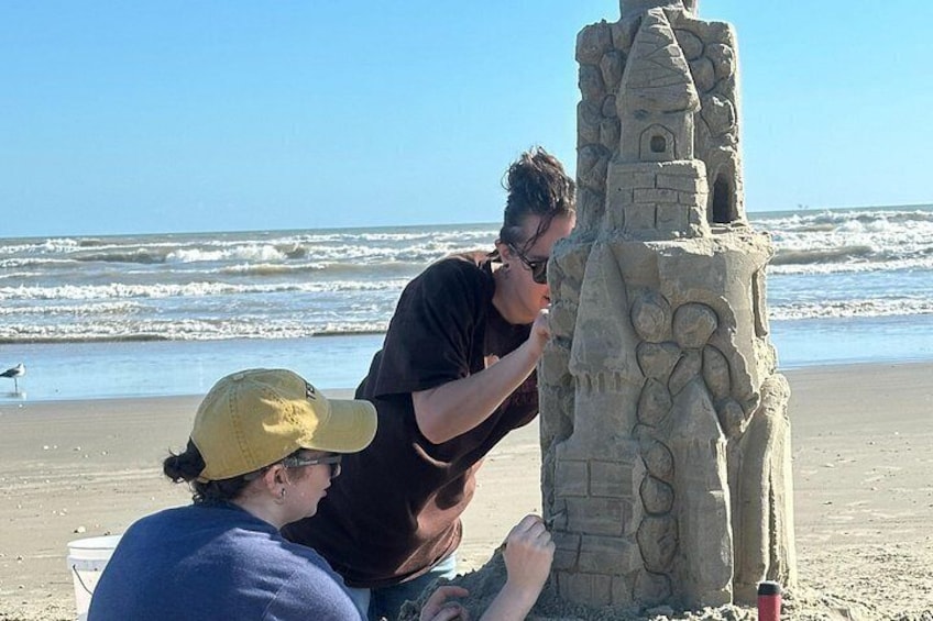 Dos personas construyen un castillo de arena en la playa, con olas al fondo. 4