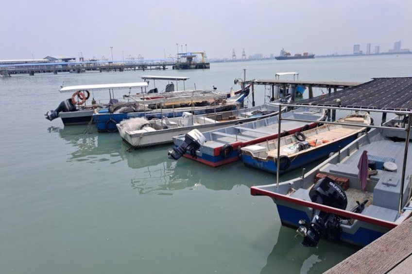 Un puerto deportivo con varias embarcaciones amarradas, un muelle que se adentra en el agua y estructuras industriales al fondo. 5