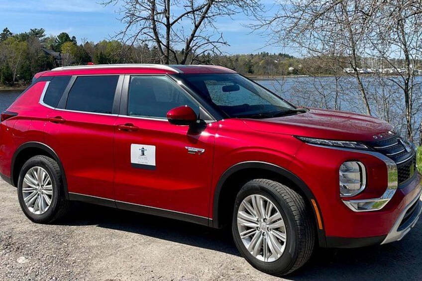 A red SUV parked by a lake with trees in the background. 2