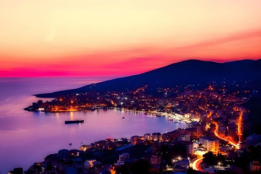 Una ciudad costera al atardecer con un muelle destacado que se adentra en el agua, una montaña al fondo y una carretera serpenteante a lo largo de la costa. 3