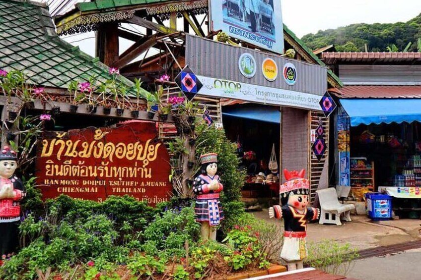 A traditional Thai market with a signboard, a statue, and a shop with a blue awning. 3
