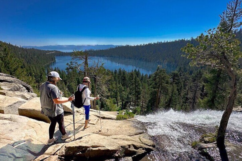 Deux randonneurs se tiennent sur un promontoire rocheux d’où l’on peut admirer un lac et une forêt. 1