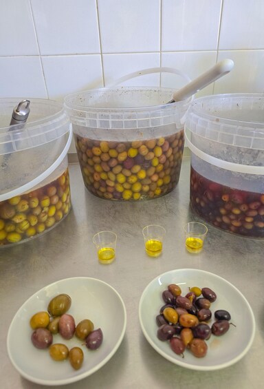 Three plastic containers with beans, two small glasses with yellow liquid, and two bowls with olives. 4