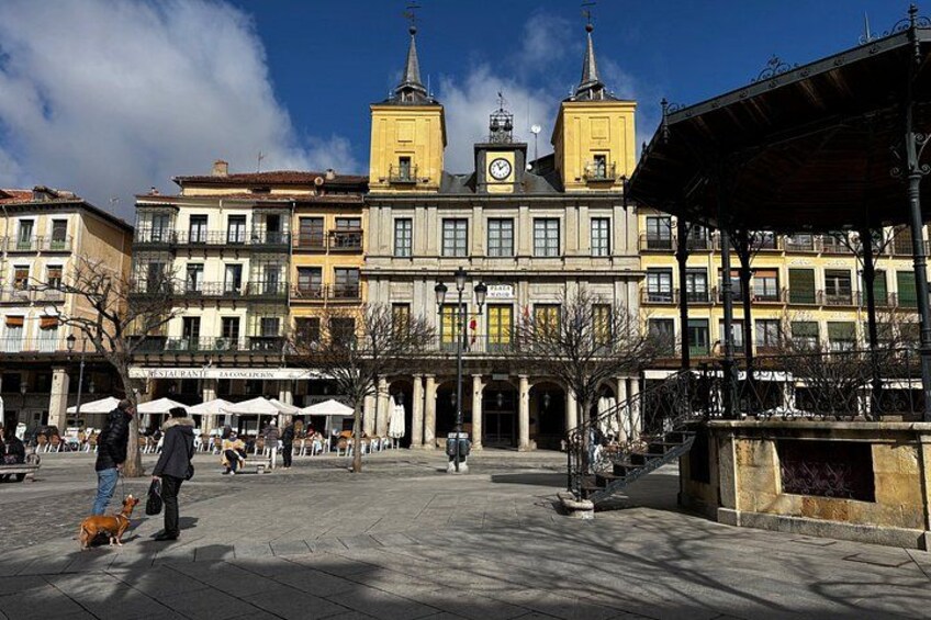A square with buildings, a clock tower, and a covered area with umbrellas. 3