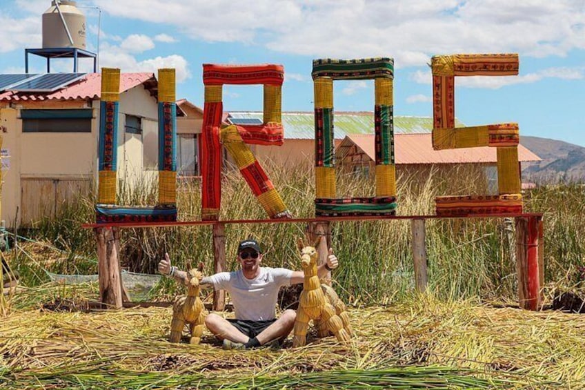 A person sitting on the ground with a large, colorful structure made of stacked materials in the background. 2