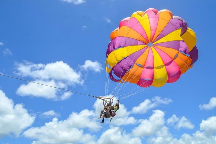 A person skydiving with a colorful parachute against a blue sky with clouds. 1