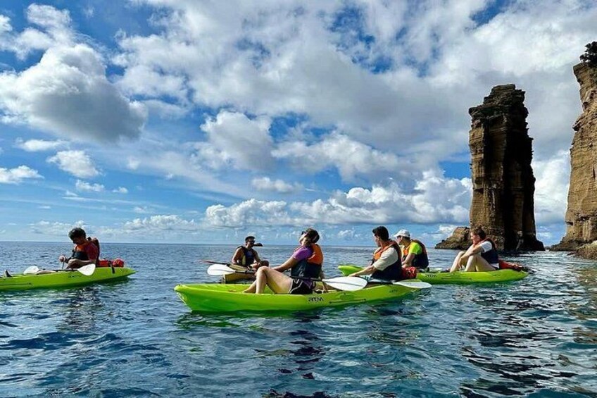 People kayaking on a calm sea with a large rock formation in the background. 2