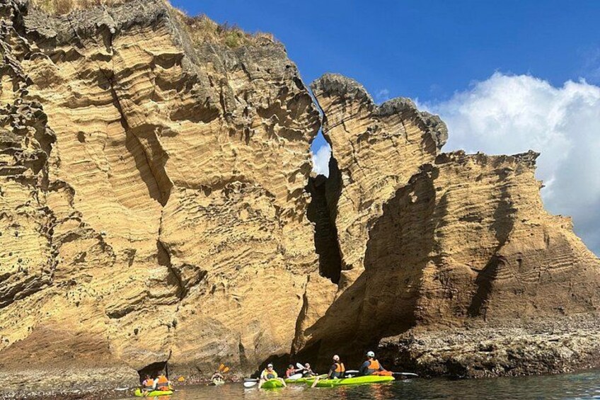 A group of kayakers on a river, a cliff with layered rock formations, and a clear blue sky. 5