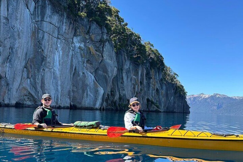 Two people in a yellow kayak on calm water with a rocky cliff in the background. 1