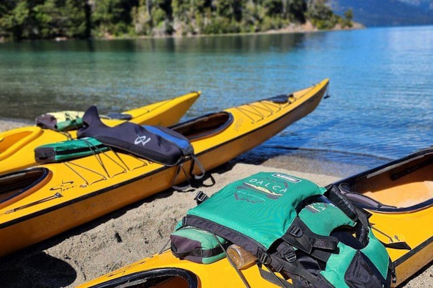 Dos kayaks amarillos en una orilla arenosa, con un lago tranquilo y árboles al fondo. 2
