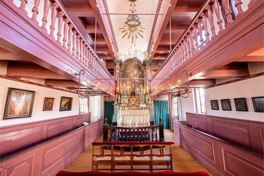A grand hall with a central altar, wooden pews, and framed pictures on the walls. 5