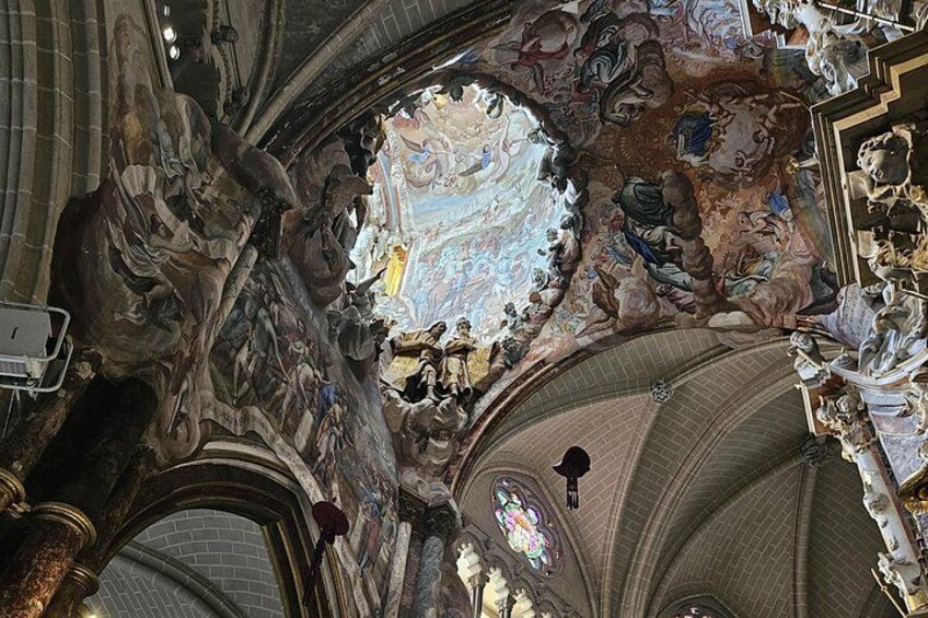 Een statig kathedraalinterieur met ingewikkelde fresco's, een groot rond raam met glas-in-lood en versierde architectuur. 2